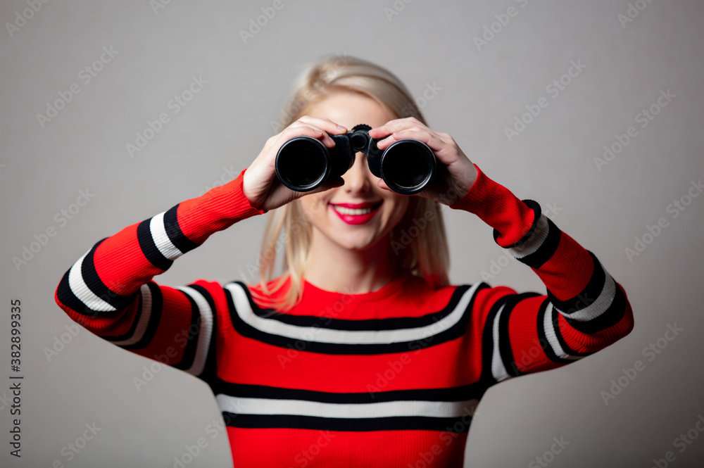 blonde in red sweater with binoculars on grey background blonde in red sweater with binoculars on grey background