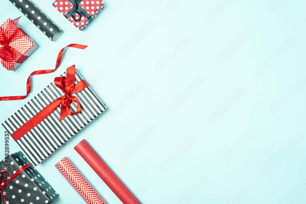Gift boxes wrapped in black and white striped, dotted and red paper with wrapping materials over a blue background. Various designs wrapped presents preparation. Copy space.