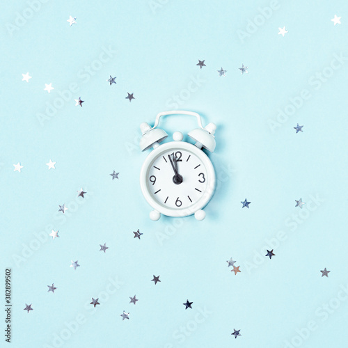 Obraz na płótnie White vintage style alarm clock showing five minutes left until midnight over blue background with silver stars sequins. New Year advent. w salonie