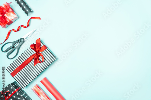 Obraz na płótnie Gift boxes wrapped in black and white striped, dotted and red paper with wrapping materials over a blue background. Various designs wrapped presents preparation. Copy space. w salonie