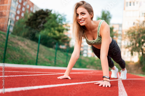 Athletic girl stands in the plank at the stadium
