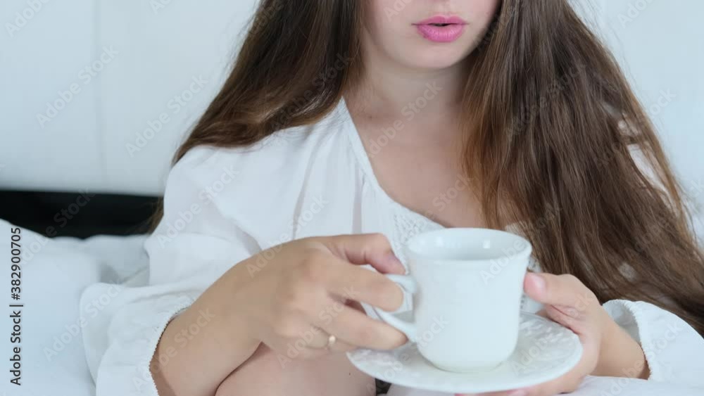 young woman in white clothes drinking tonic coffee, tea from a cup in bed, lush long hair, beauty and health concept, lifestyle, cozy home young woman in white clothes drinking tonic coffee, tea from a cup in bed, lush long hair, beauty and health concept, lifestyle, cozy home