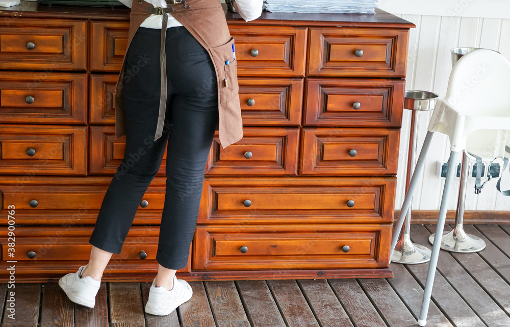 a waitress in an apron, jeans and white sneakers stands at the camod