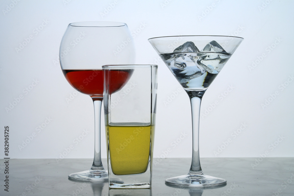 Three clear crystal glasses of different shape located at the empty background. Beautiful cocktail set with ice at the bar. Three clear crystal glasses of different shape located at the empty background. Beautiful cocktail set with ice at the bar.