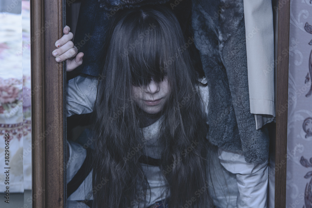 Mad scary girl in cupboard at dark night. Horror background with child possessed by devil. Demon possessed little girl in closet at night. Ghost of little girl at dark night. Child ghost in cupboard. Mad scary girl in cupboard at dark night. Horror background with child possessed by devil. Demon possessed little girl in closet at night. Ghost of little girl at dark night. Child ghost in cupboard.