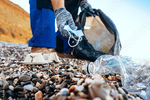 Man volunteer collecting used medical masks on the beach near the ocean