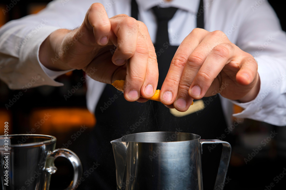 bartender in a black apron holds an orange peel 
