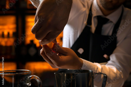 bartender in a black apron holds an orange peel 