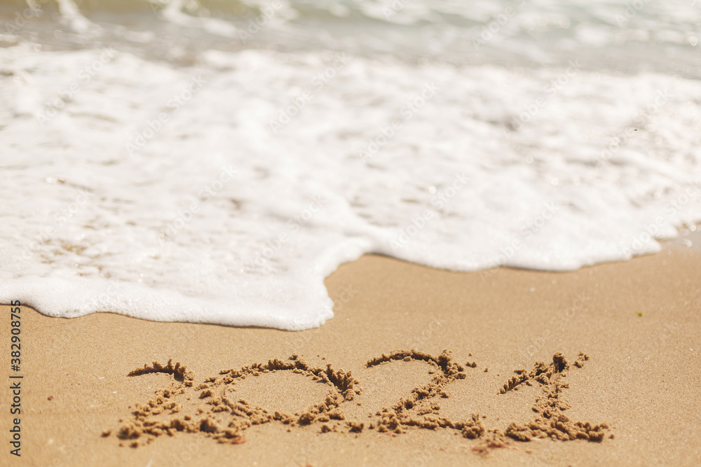 Hello 2021! Happy new year 2021 sign handwritten on sandy beach with waves and white foam Hello 2021! Happy new year 2021 sign handwritten on sandy beach with waves and white foam