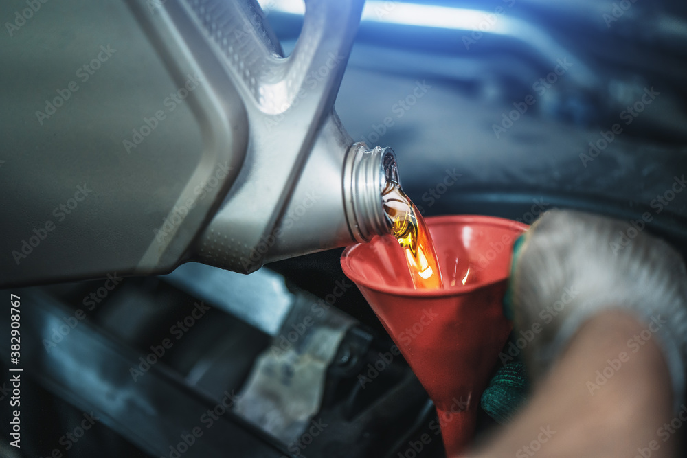 Worker pours new synthetic motor oil from canister into funnel at car service, regular oil change - auto health concept.