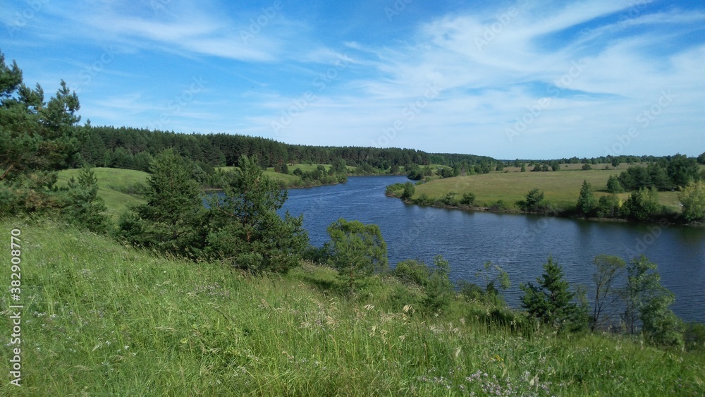  Beautiful summer sunny landscape. River among meadows and forests, blue sky in the clouds. Mountainous terrain.