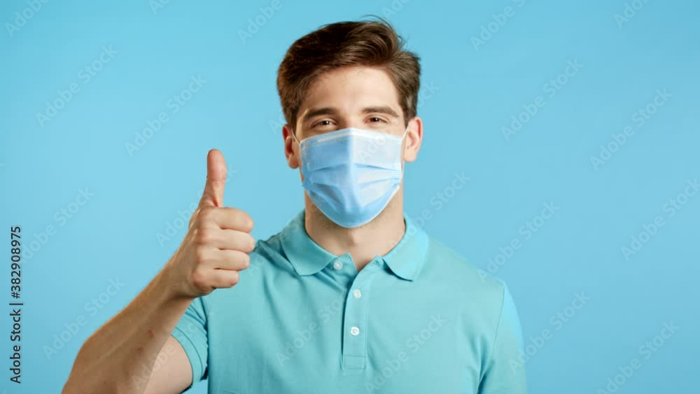 Handsome young man in protective medical mask showing thumbs up, like sign over studio background. Winner. Success. Body language. Handsome young man in protective medical mask showing thumbs up, like sign over studio background. Winner. Success. Body language.