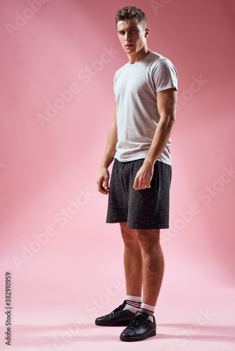 A man in sports shorts in a T-shirt and sneakers on a pink background in full growth