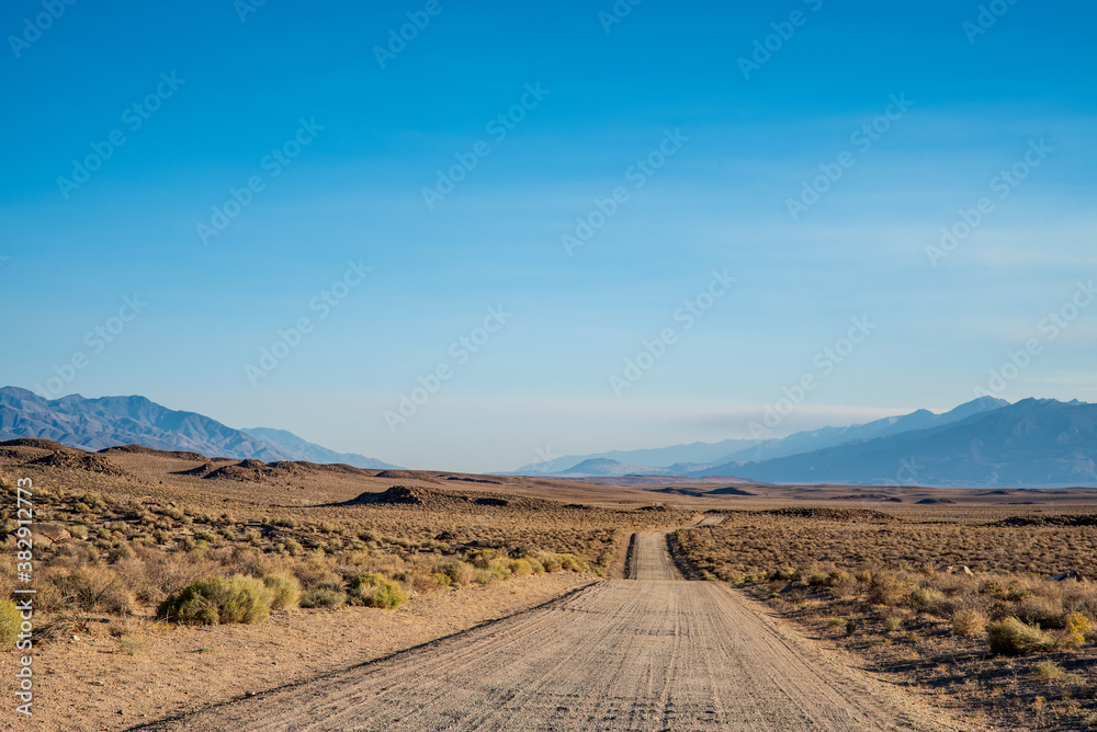 dirt road in desert valley heading toward distant mountains in California 