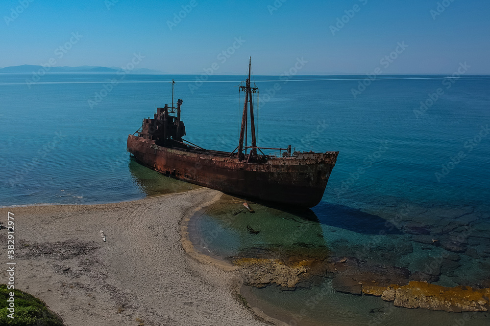 Aerial photo of Dimitrios shipwreck in  Gythio, Greece. A partially sunk rusty metal shipwreck decaying through time on a sandy beach on a sunny day. Famous shipwreck in greece.