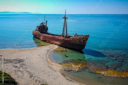 Aerial photo of Dimitrios shipwreck in Gythio, Greece. A partially sunk rusty metal shipwreck decaying through time on a sandy beach on a sunny day. Famous shipwreck in greece.