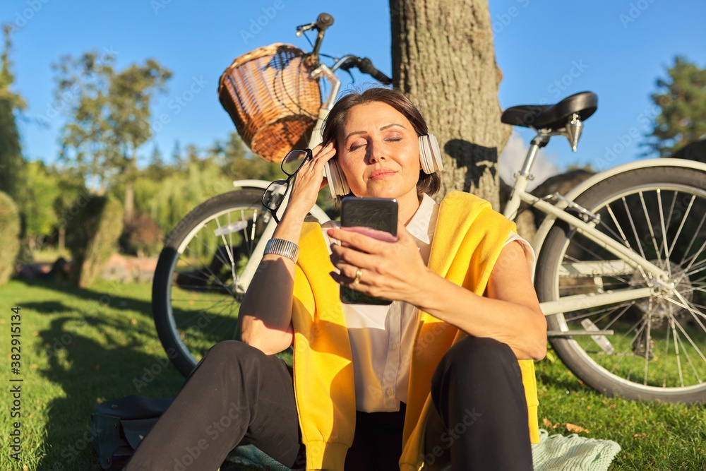 Obraz premium Happy mature woman with closed eyes headphones sitting in the park