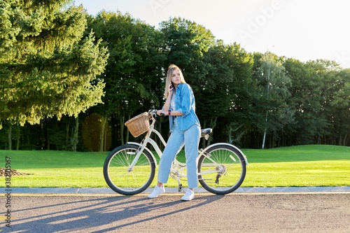 Young beautiful happy woman on the road with bike talking on smartphone