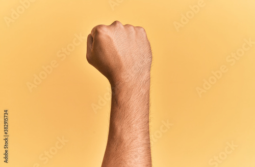 Arm and hand of caucasian man over yellow isolated background doing protest and revolution gesture, fist expressing force and power