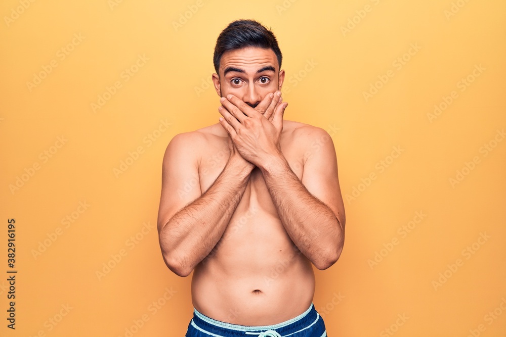 Young handsome man with beard wearing sleeveless t-shirt standing over yellow background shocked covering mouth with hands for mistake. Secret concept.