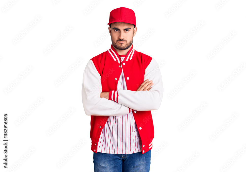 Young handsome man wearing baseball jacket and cap skeptic and nervous, disapproving expression on face with crossed arms. negative person. Young handsome man wearing baseball jacket and cap skeptic and nervous, disapproving expression on face with crossed arms. negative person.