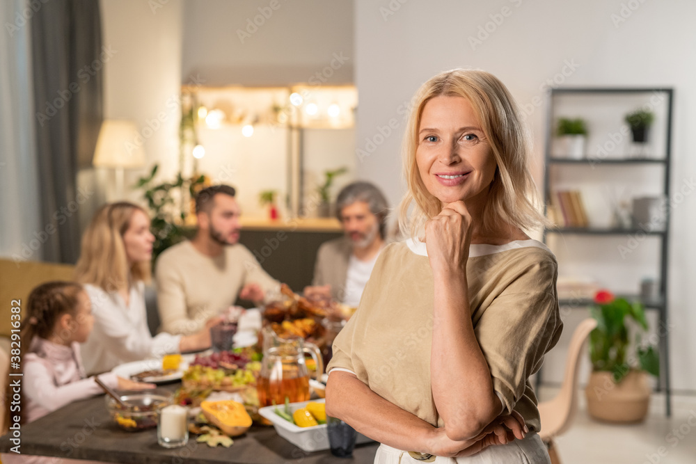 Happy mature female standing in front of camera against large family dining