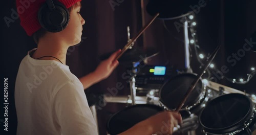 Cool and talented young boy playing drums in white tshirt performing song in dark background feeling super star on stage. Teenager rock band drummer
