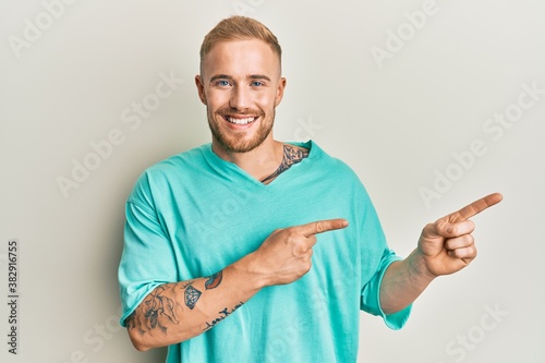 Young caucasian man wearing casual clothes smiling and looking at the camera pointing with two hands and fingers to the side.