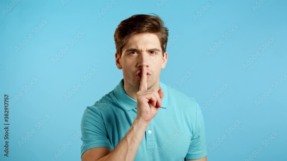 Handsome man in blue holding finger on lips over studio background. Gesture of shhh, secret, silence. Close up. Handsome man in blue holding finger on lips over studio background. Gesture of shhh, secret, silence. Close up.