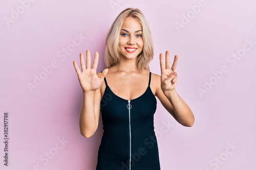 Beautiful caucasian blonde girl wearing sexy party dress showing and pointing up with fingers number eight while smiling confident and happy.