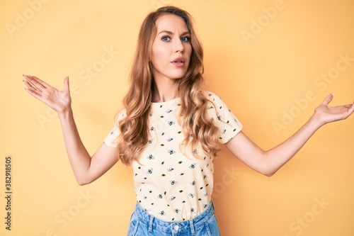 Young caucasian woman with blond hair wearing casual summer clothes clueless and confused with open arms, no idea and doubtful face.