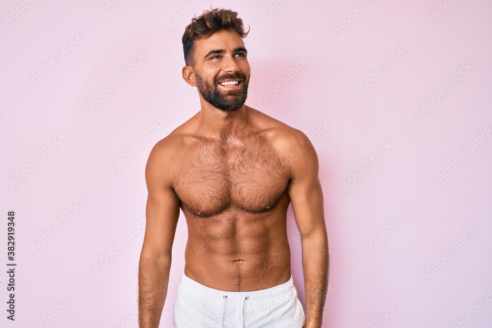 Young hispanic man standing shirtless looking away to side with smile on face, natural expression. laughing confident. Young hispanic man standing shirtless looking away to side with smile on face, natural expression. laughing confident.