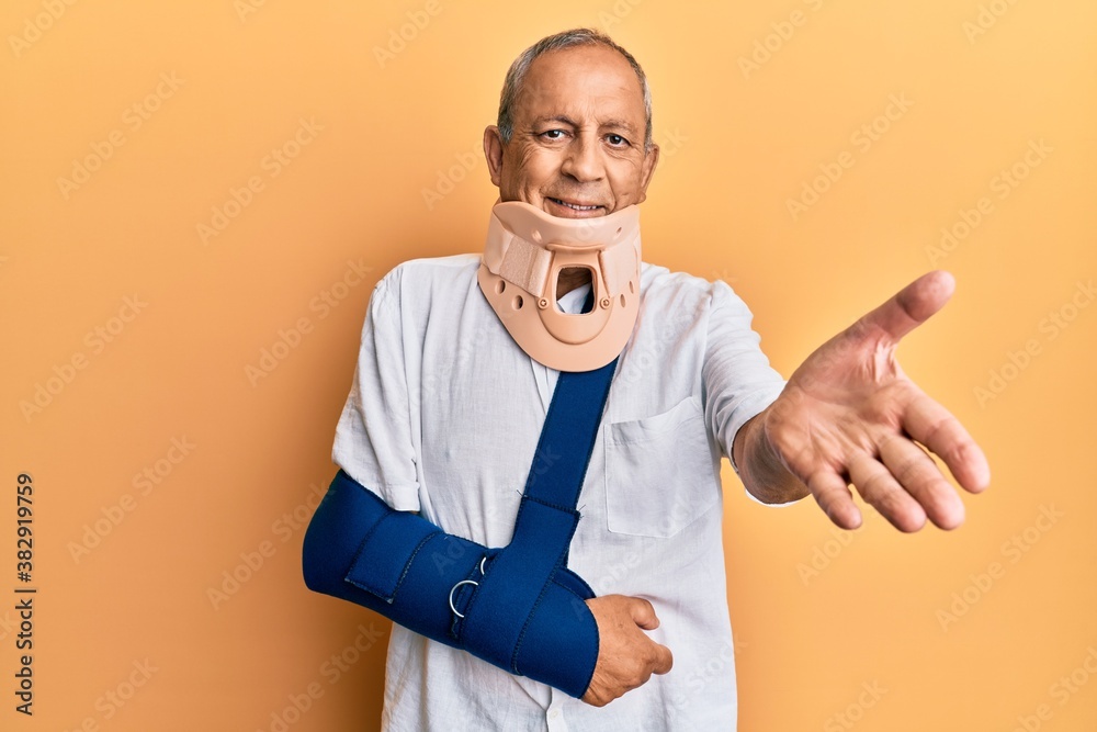 Handsome mature senior man wearing cervical collar and arm on sling smiling cheerful offering palm hand giving assistance and acceptance. Handsome mature senior man wearing cervical collar and arm on sling smiling cheerful offering palm hand giving assistance and acceptance.