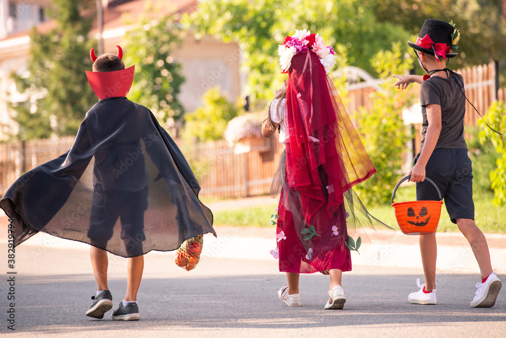 Back view of three friendly children in halloween costumes carrying sweet treats