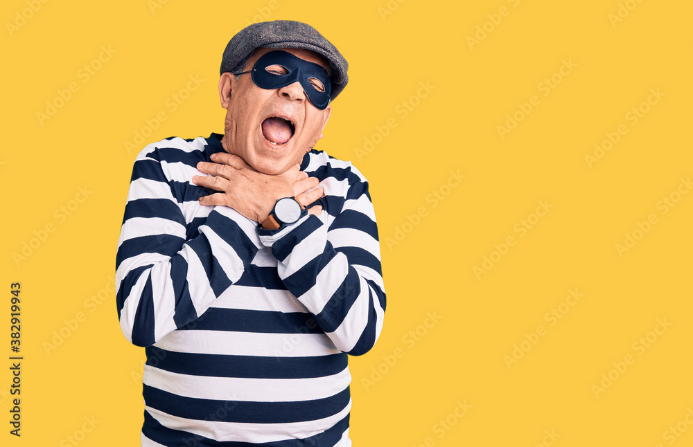 Senior handsome man wearing burglar mask and t-shirt shouting suffocate because painful strangle. health problem. asphyxiate and suicide concept. Senior handsome man wearing burglar mask and t-shirt shouting suffocate because painful strangle. health problem. asphyxiate and suicide concept.
