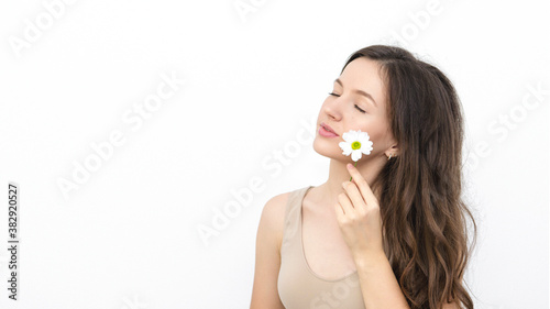 young woman holds a camomile near her face