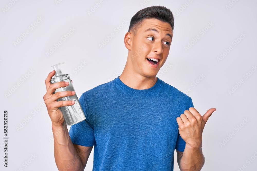 Young hispanic boy using hand sanitizer gel pointing thumb up to the side smiling happy with open mouth Young hispanic boy using hand sanitizer gel pointing thumb up to the side smiling happy with open mouth