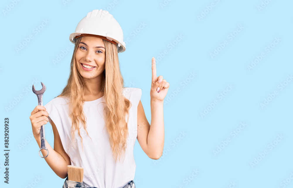 Beautiful caucasian woman with blonde hair wearing hardhat and builder clothes surprised with an idea or question pointing finger with happy face, number one Beautiful caucasian woman with blonde hair wearing hardhat and builder clothes surprised with an idea or question pointing finger with happy face, number one
