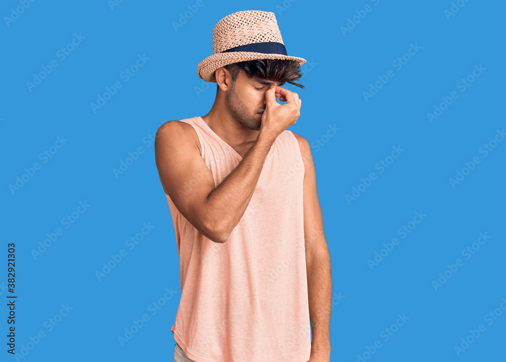 Young hispanic man wearing summer hat tired rubbing nose and eyes feeling fatigue and headache. stress and frustration concept. Young hispanic man wearing summer hat tired rubbing nose and eyes feeling fatigue and headache. stress and frustration concept.