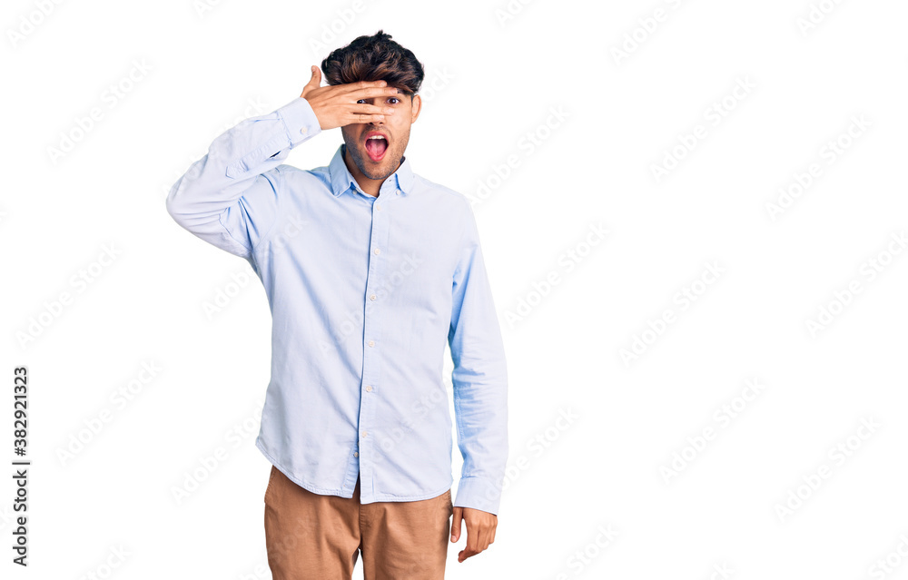 Young hispanic man wearing casual shirt peeking in shock covering face and eyes with hand, looking through fingers with embarrassed expression. Young hispanic man wearing casual shirt peeking in shock covering face and eyes with hand, looking through fingers with embarrassed expression.