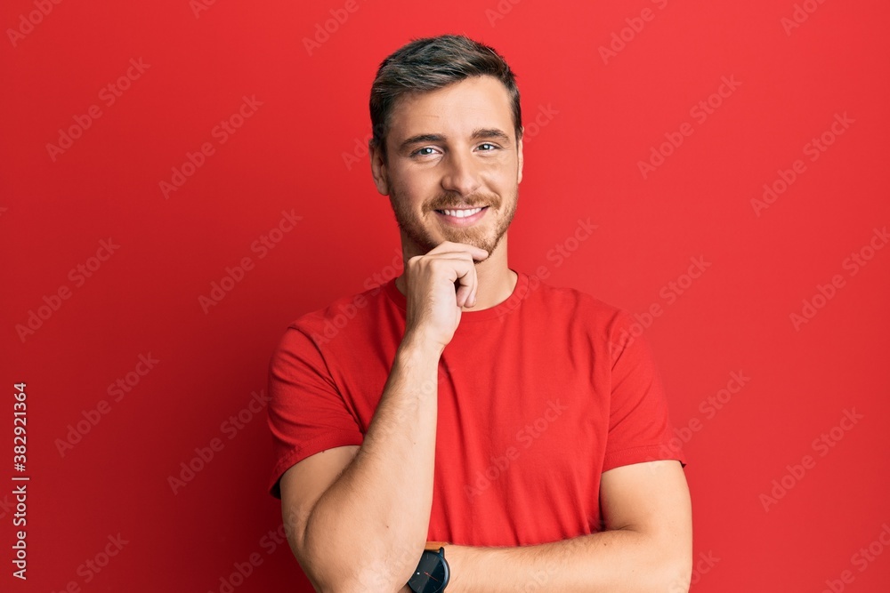 Handsome caucasian man wearing casual red tshirt looking confident at the camera smiling with crossed arms and hand raised on chin. thinking positive. Handsome caucasian man wearing casual red tshirt looking confident at the camera smiling with crossed arms and hand raised on chin. thinking positive.