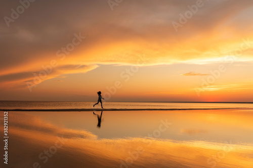 Silhouette of fitness woman running on the beach at sunset. Copy space. 