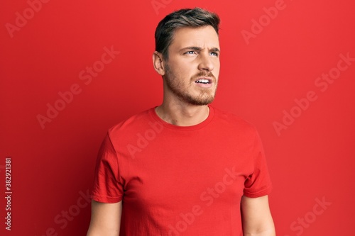 Handsome caucasian man wearing casual red tshirt angry and mad screaming frustrated and furious, shouting with anger. rage and aggressive concept.