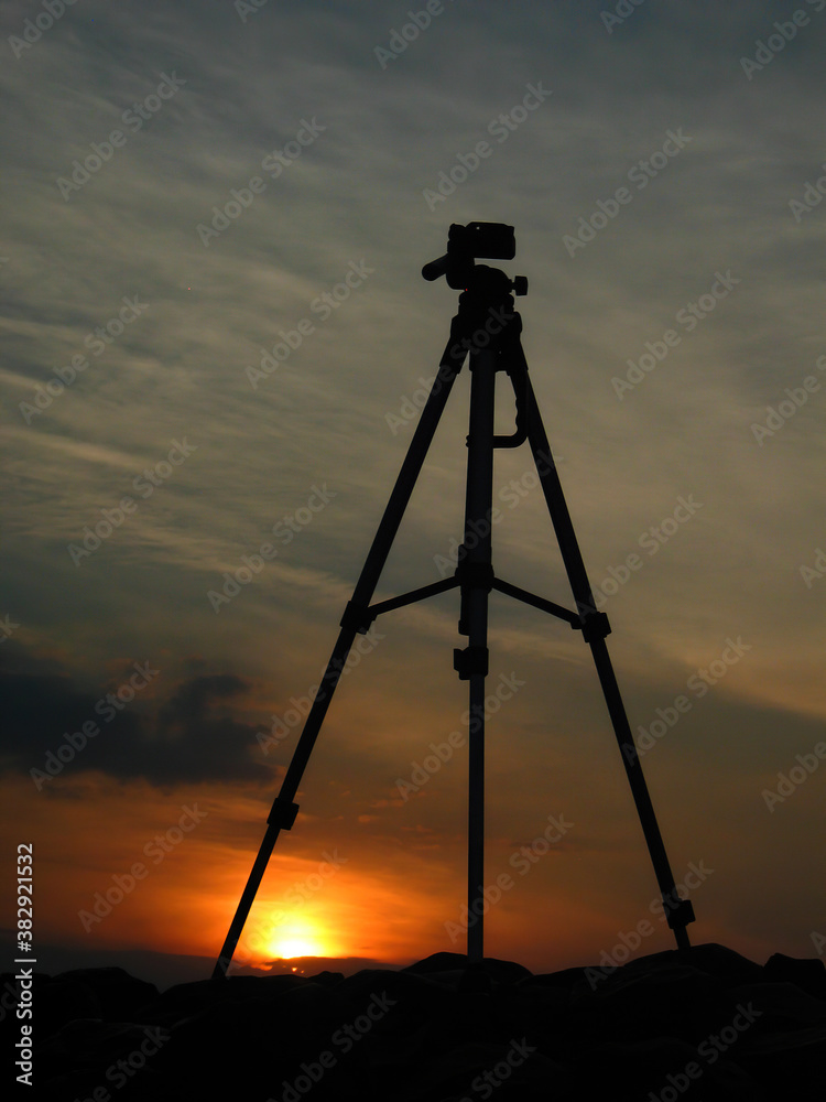 Silhouette of a tripod on top of a basalt mountain.Scenery with silhouettes over the valley at sunset on the horizon.