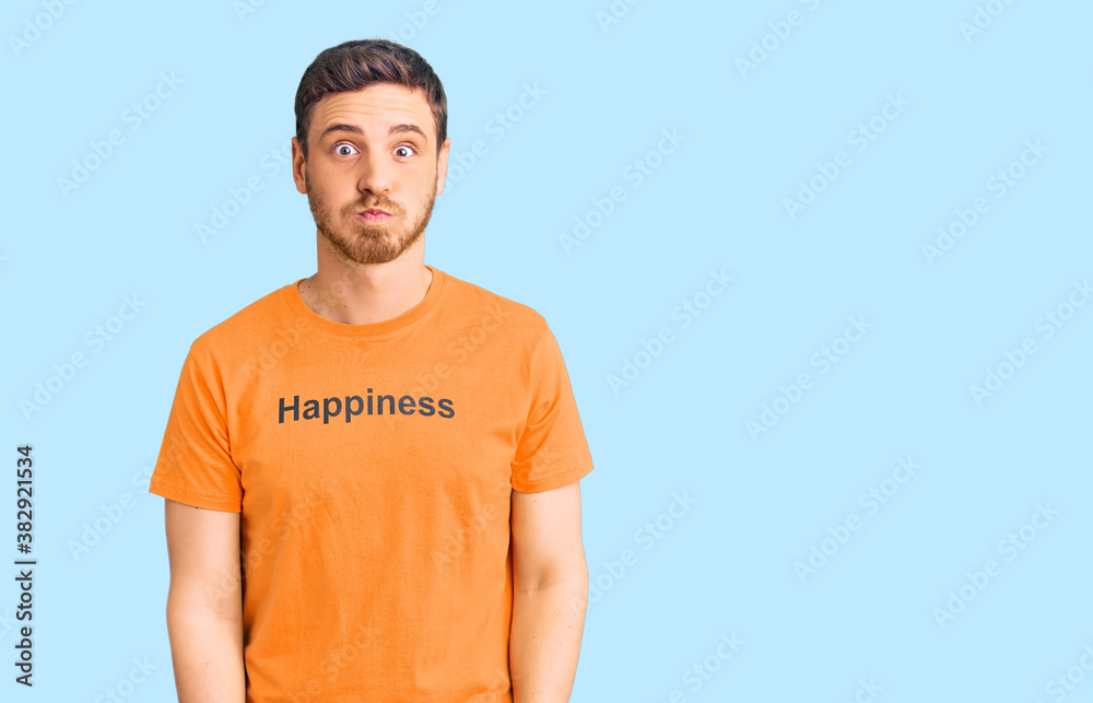Handsome young man with bear wearing tshirt with happiness word message puffing cheeks with funny face. mouth inflated with air, crazy expression. Handsome young man with bear wearing tshirt with happiness word message puffing cheeks with funny face. mouth inflated with air, crazy expression.
