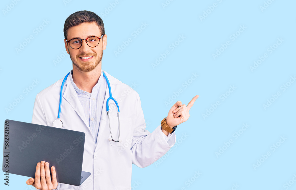 Handsome young man with bear wearing doctor uniform working using computer laptop smiling happy pointing with hand and finger to the side Handsome young man with bear wearing doctor uniform working using computer laptop smiling happy pointing with hand and finger to the side