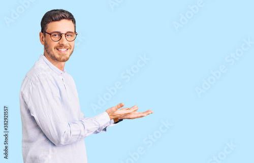 Handsome young man with bear wearing elegant business shirt and glasses pointing aside with hands open palms showing copy space, presenting advertisement smiling excited happy
