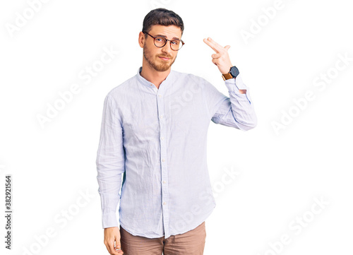 Photography Handsome young man with bear wearing elegant business shirt and glasses shooting and killing oneself pointing hand and fingers to head like gun, suicide gesture
