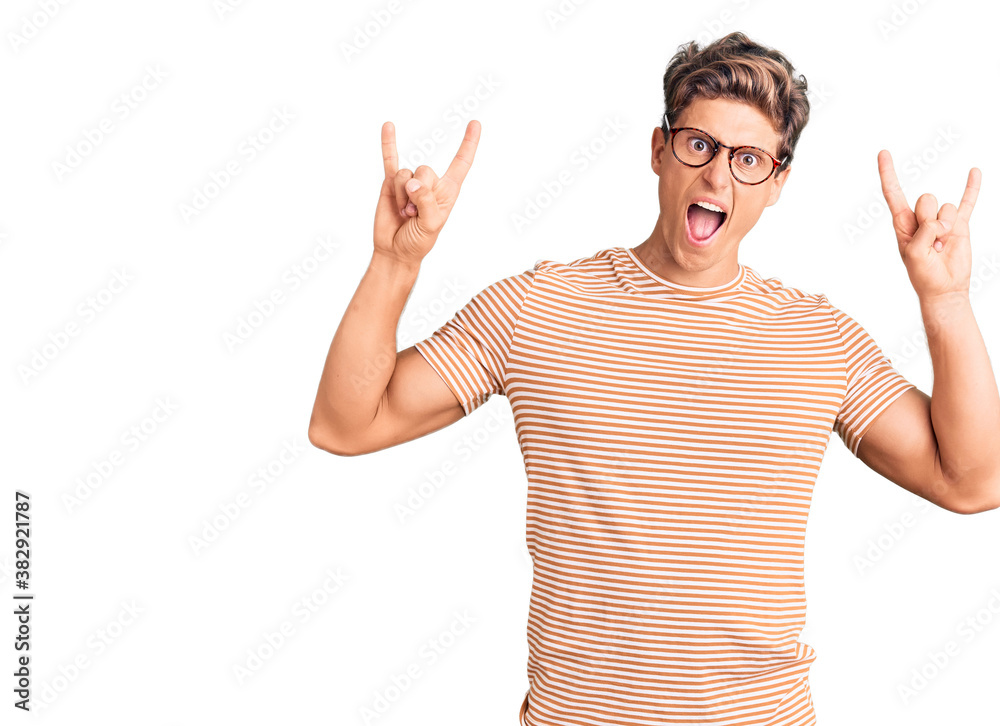 Naklejka premium Young handsome man wearing casual clothes and glasses shouting with crazy expression doing rock symbol with hands up. music star. heavy concept.