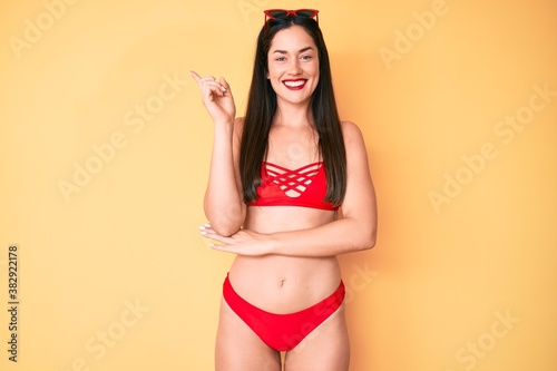 Young beautiful caucasian woman wearing bikini smiling happy pointing with hand and finger to the side